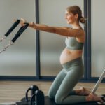 Pregnant woman exercising with the help of reformer on pilates class